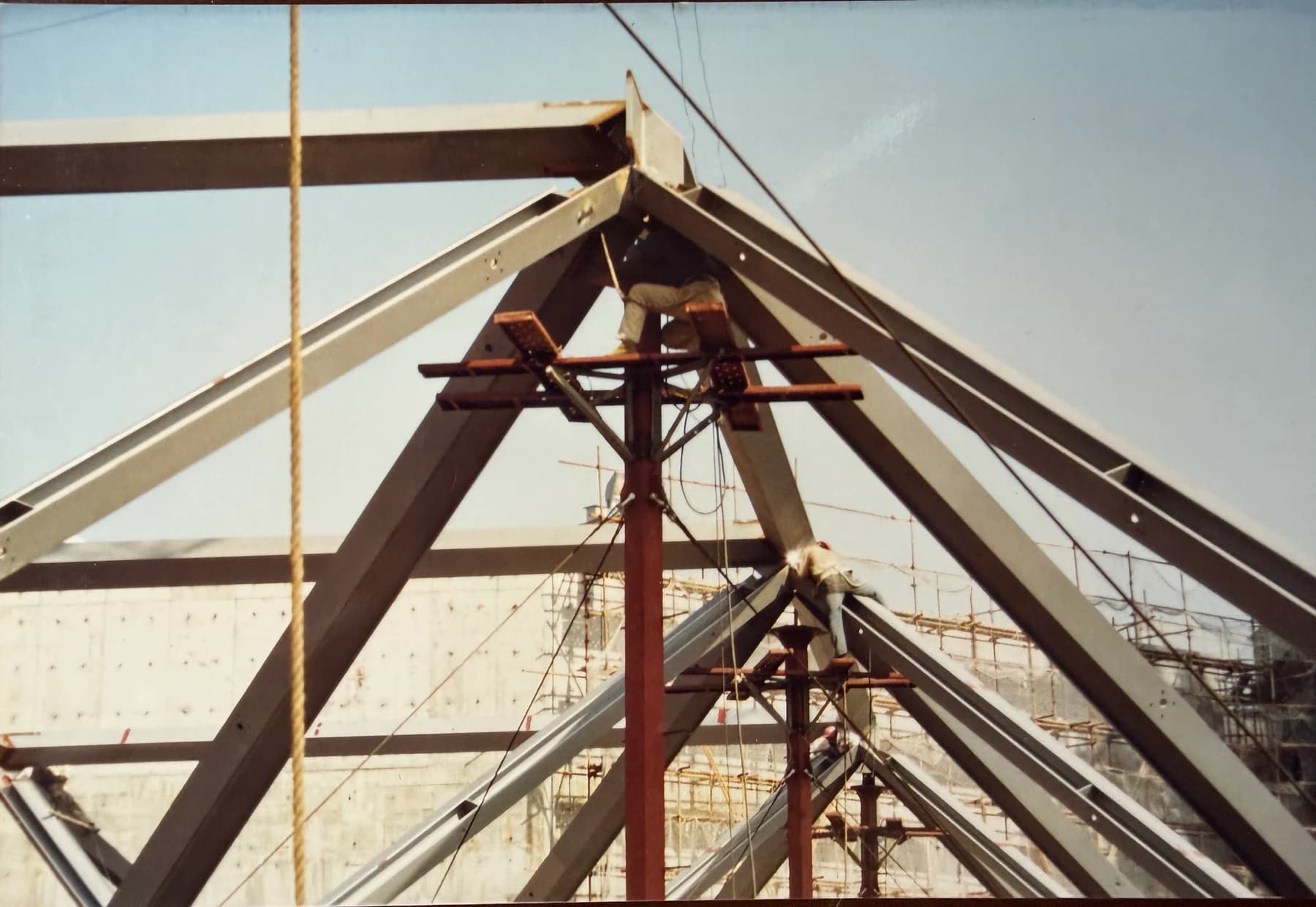 Workers assembling the apex connections of repeating pyramidal steel roof frames above a hotel atrium