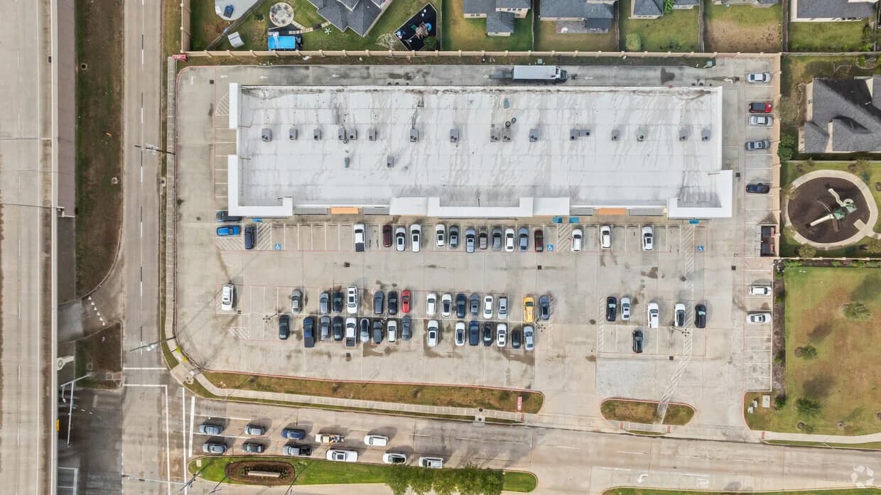 Top-down aerial view of a shopping center building, parking, and site circulation
